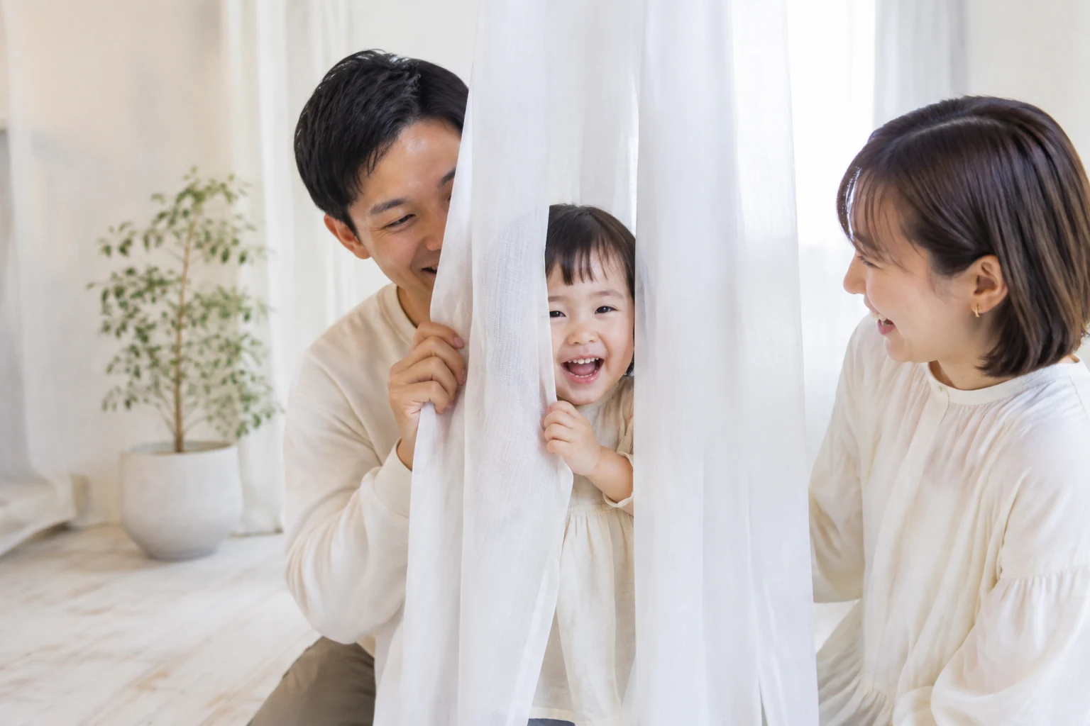 白いカーテンでいないいないばあをして遊ぶ親子