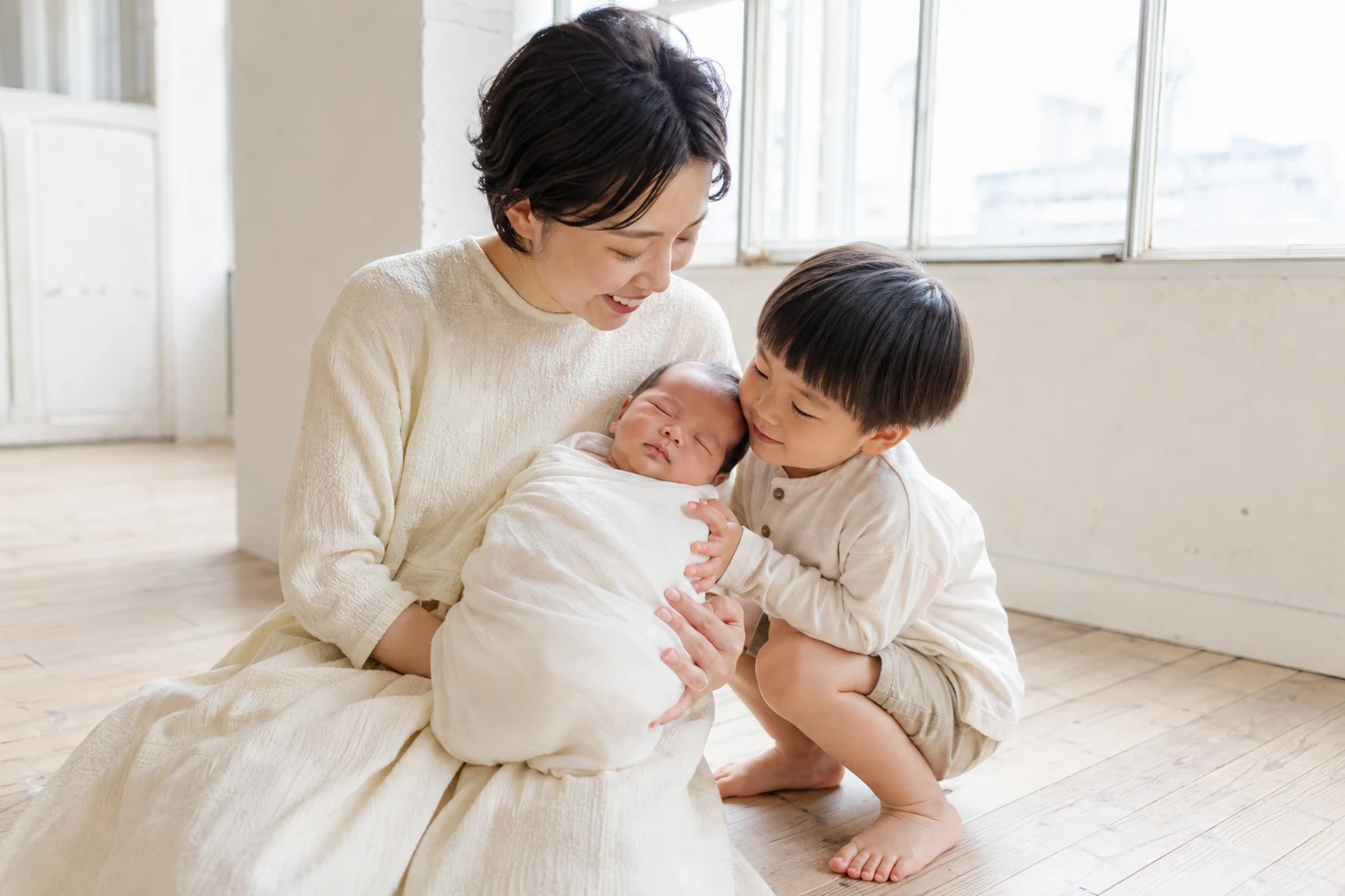お母さんの腕で眠る赤ちゃんをのぞき込むきょうだい